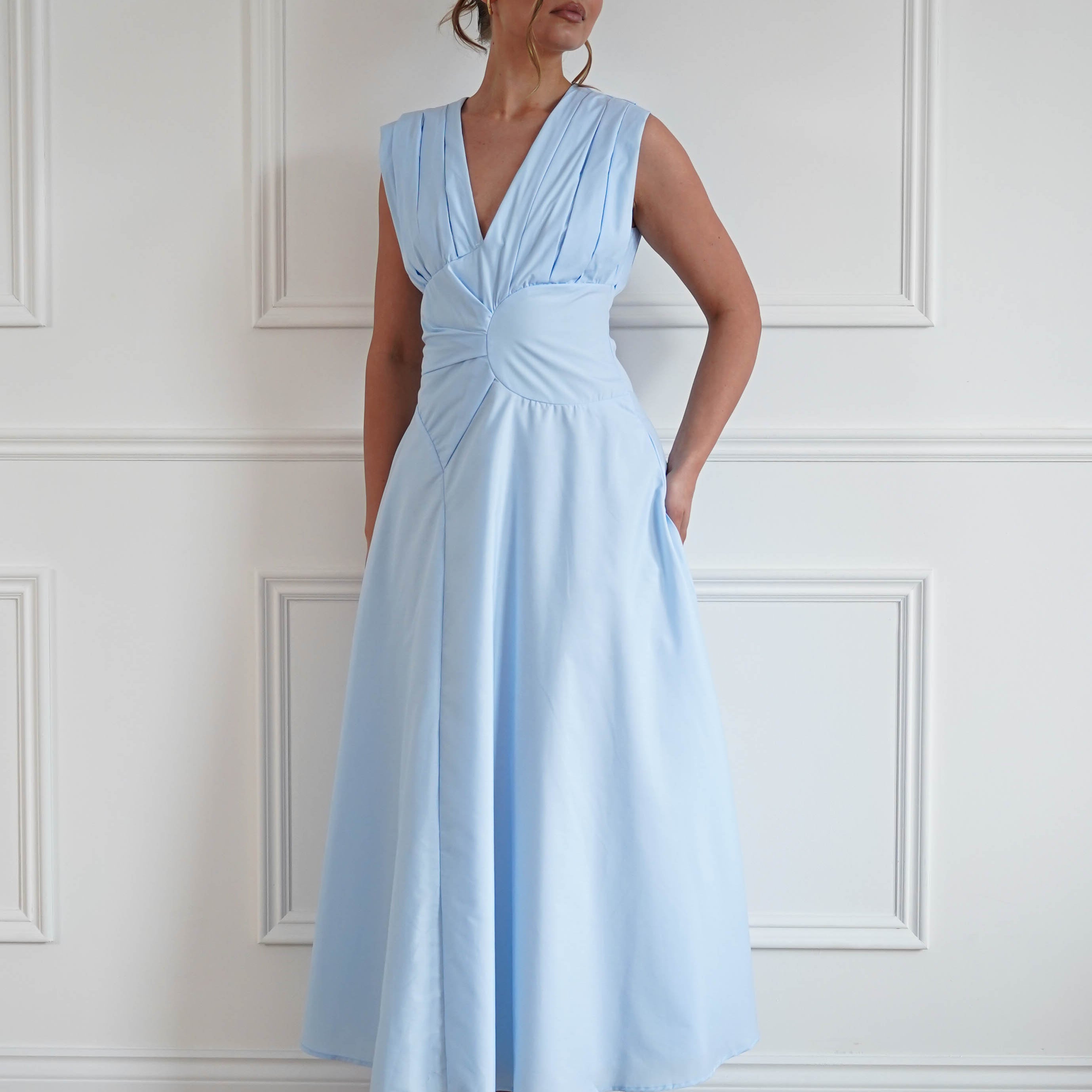 Woman wearing a baby blue midi dress with a sleeveless V-neckline, twist waist detailing, and a flowing A-line skirt, perfect for weddings, garden parties, baby showers, and special occasions.