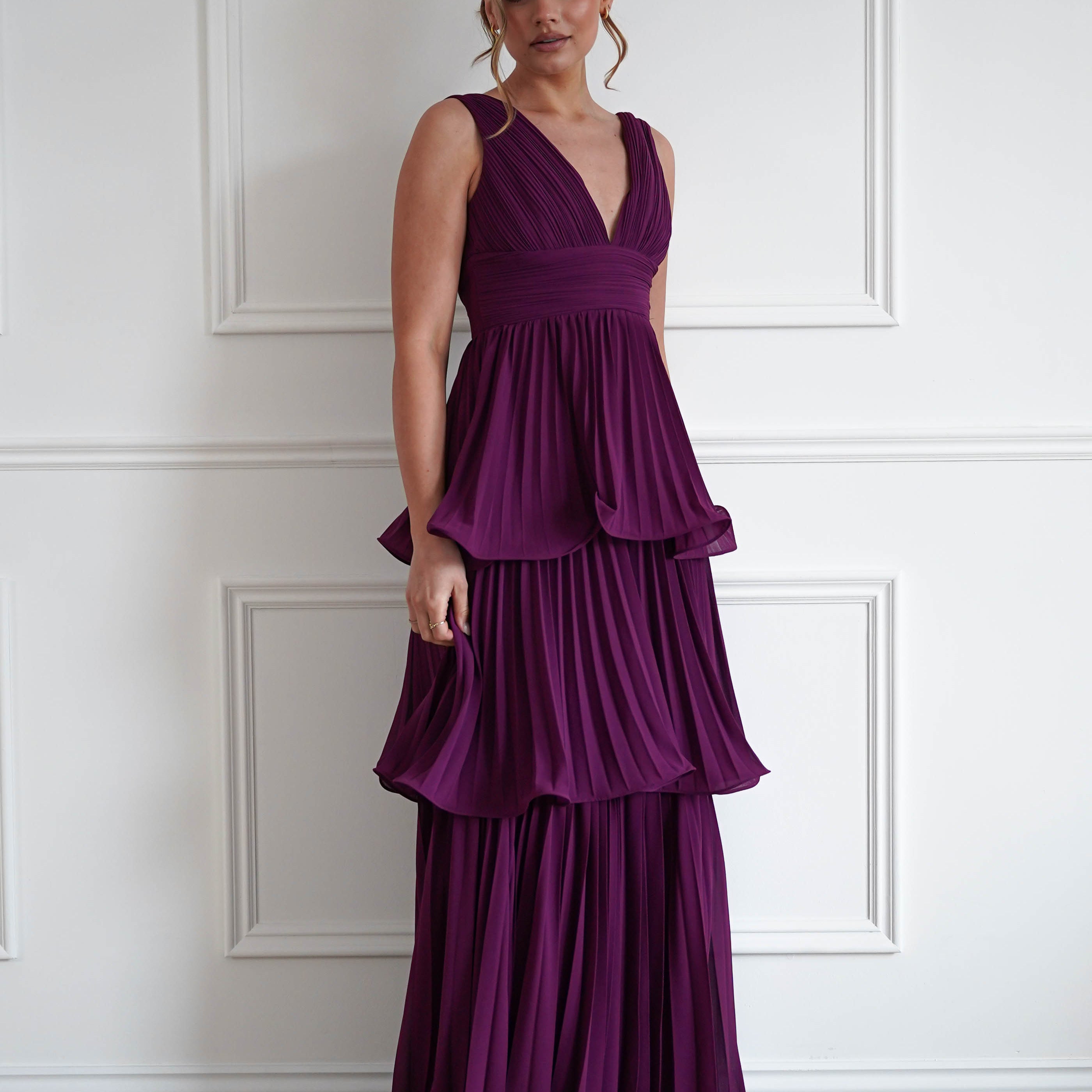 Woman wearing the Vina tiered pleated layered maxi dress in plum with a deep V-neckline, flowing pleated tiers, and floor-length elegant silhouette.