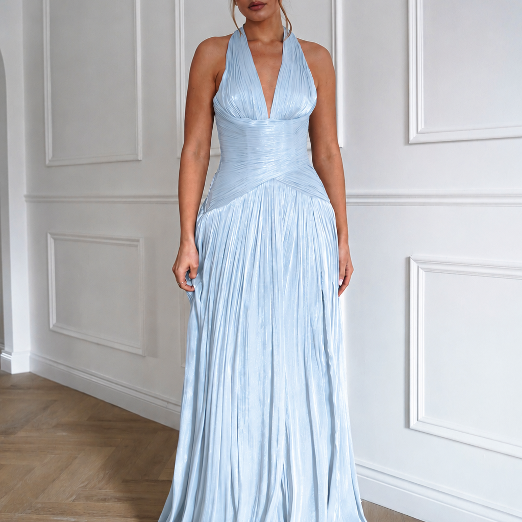 Woman wearing a light blue halter neck gown standing against a white paneled wall.