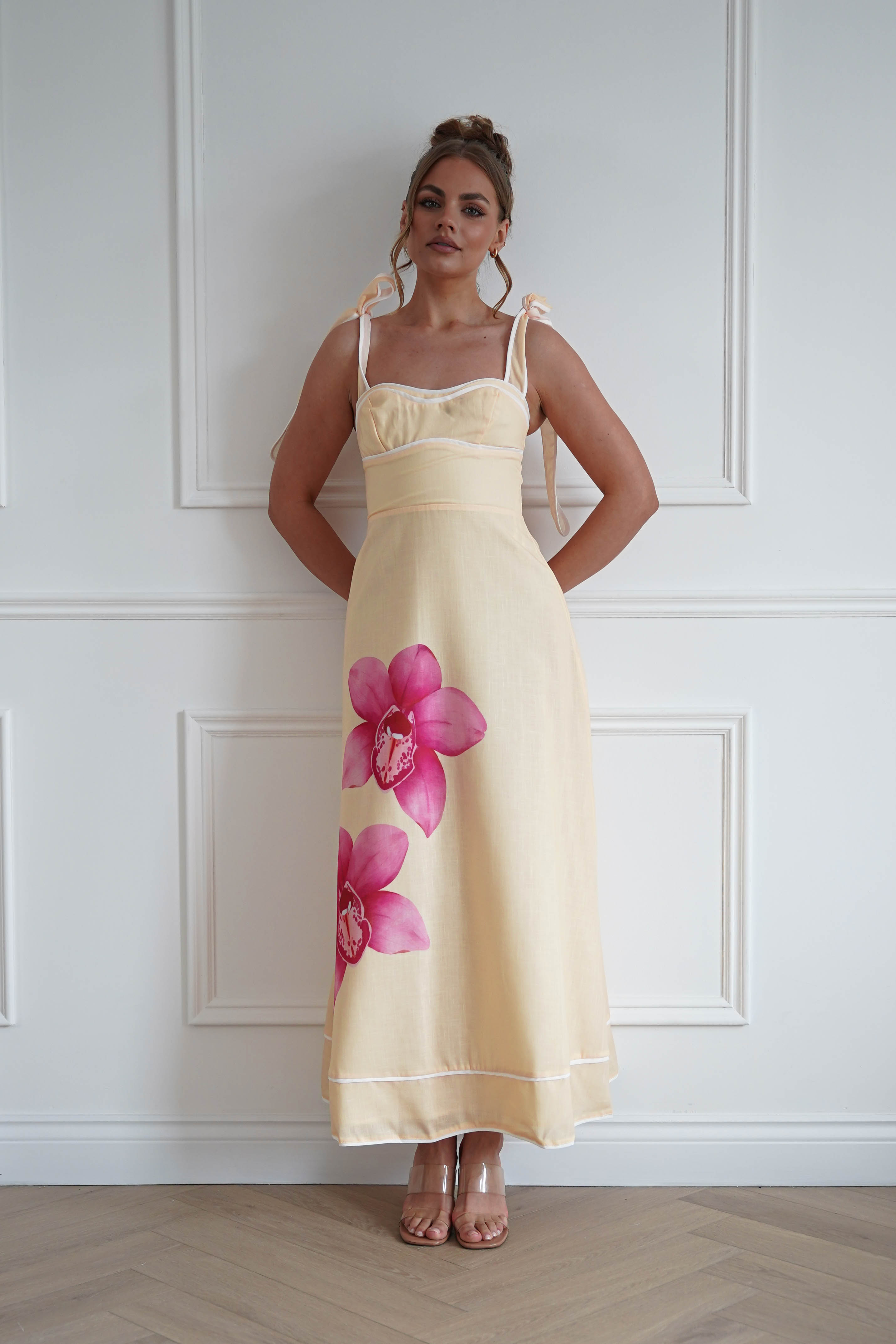 Woman wearing a yellow floral maxi dress with a sweetheart neckline, adjustable tie straps, and a flowing skirt featuring bold pink orchid prints, perfect for holidays, garden parties, summer weddings, and special occasions.