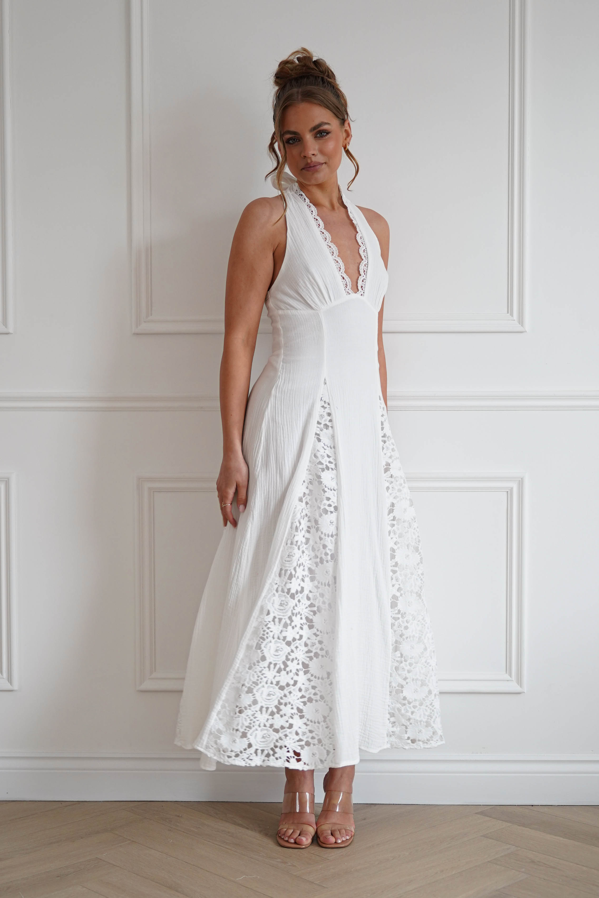 Woman wearing a white midi dress with a halterneck neckline, delicate lace trim detailing, textured fabric, and a flowing A-line skirt, perfect for bridal showers, engagement parties, holidays, and summer special occasions.